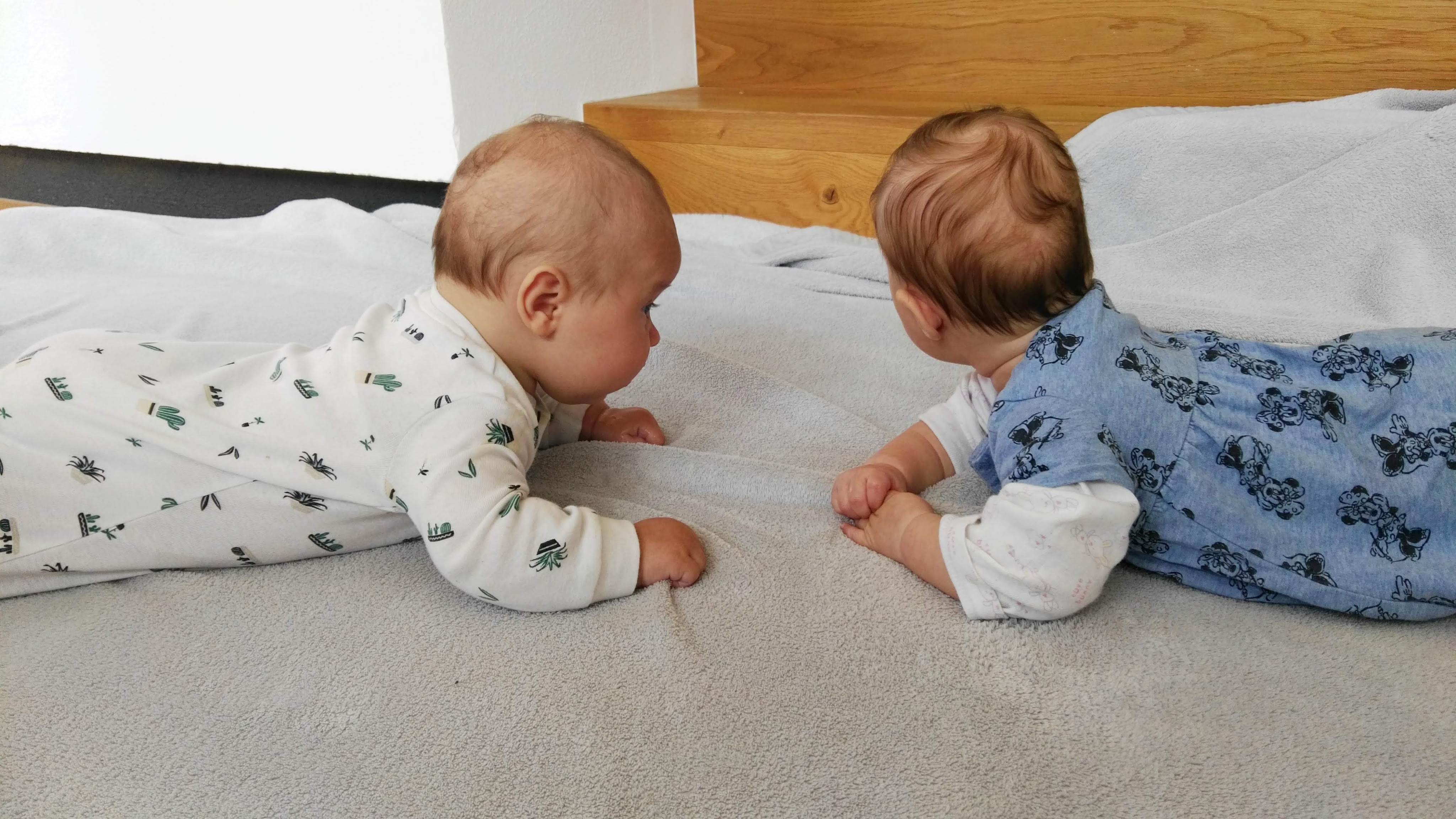 2 Babys liegen am Bauch und sehen sich an